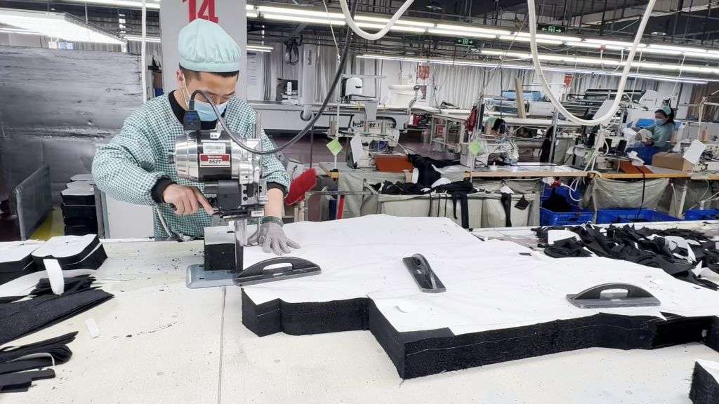 Worker using Eastman straight knife cutting machine for layered fabric cutting at Newasia Garment factory