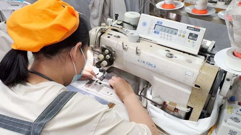 Worker operating JUKI industrial sewing machine at clothing manufacturer in China factory