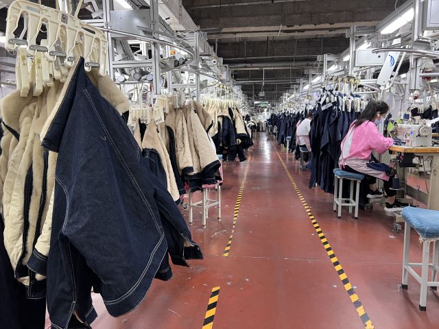 Garment factory production line showing sewing workers assembling denim and apparel in bulk manufacturing process