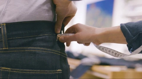 Waistband measurement on denim jeans showing precise flat measurement technique and tolerance control
